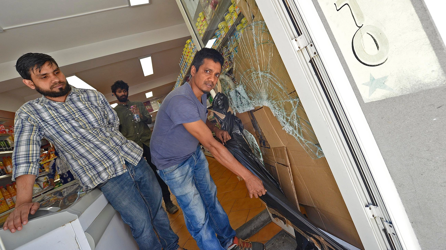Il titolare del negozio Uddin Shohel davanti alla vetrata spaccata con un tombino